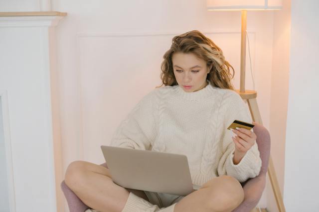 A woman sits on a chair and enters her credit card information on her laptop.