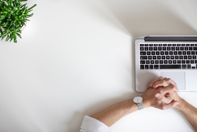 A person wearing a watch sits in front of a laptop.