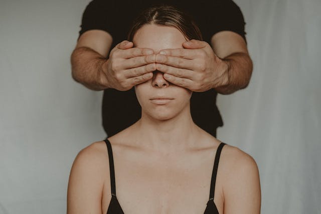 A man covers a woman’s eyes with his hands.