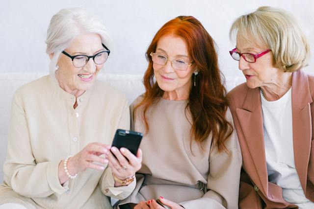 Three elderly women browse videos on a phone.