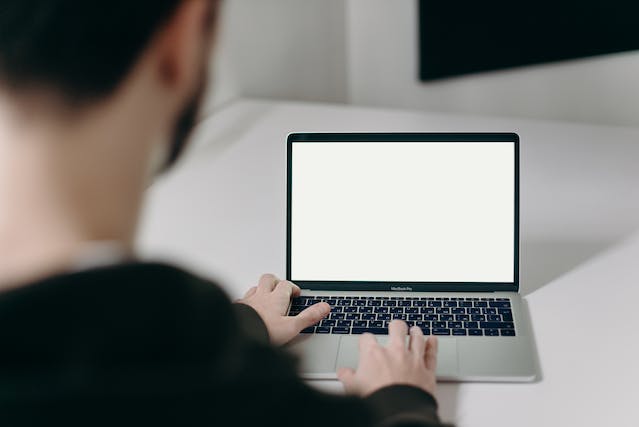 A man scrolls through his laptop, which shows a blank screen.