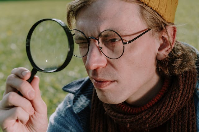 A man wearing glasses holds a magnifying glass up to one eye.