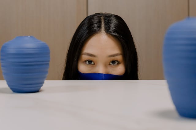 A woman in a blue face mask peeks over a table.