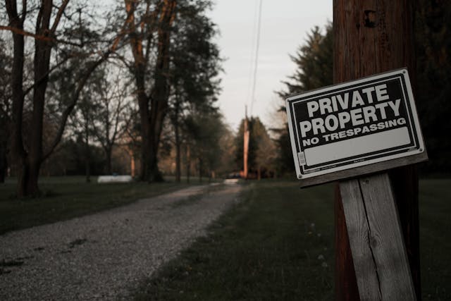 A wooden sign that reads, “Private property, no trespassing,” stands beside a private road.