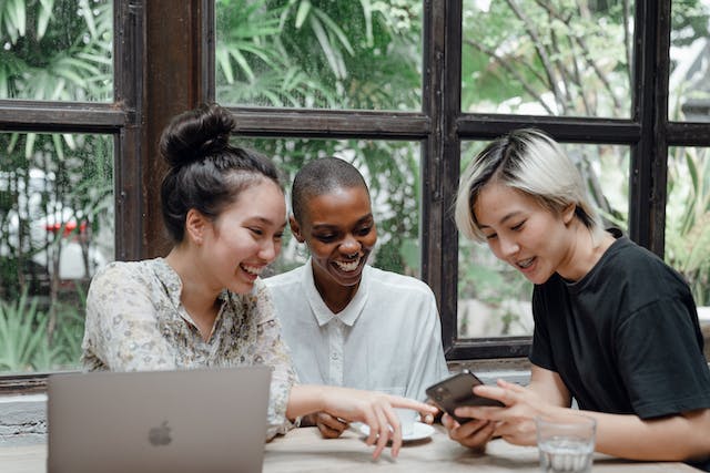 Three friends sit around a table watching TikTok videos.