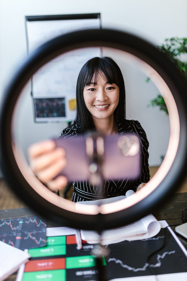A woman smiles as she puts her cellphone in front of a ring light.