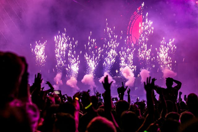 A big audience cheers as fireworks go off onstage at a concert.