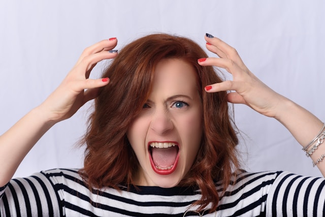 A woman screams and has her hands hovering over her head.
