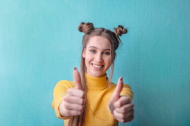 A young woman in a yellow sweater gives two thumbs up.