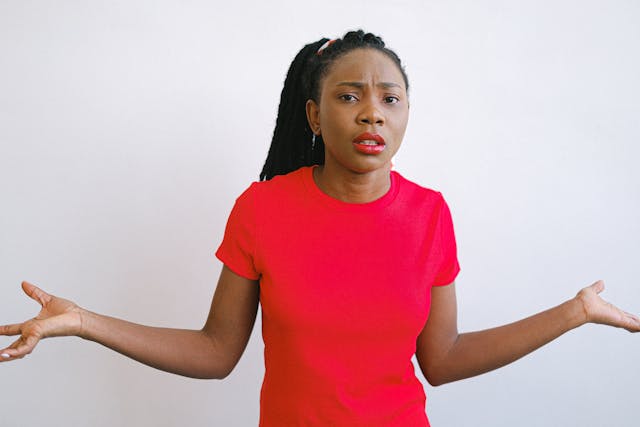 A woman looks confused as she holds her arms out to the sides and shrugs.