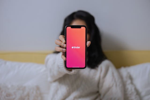 A woman holds a phone with “Tinder” on the screen.