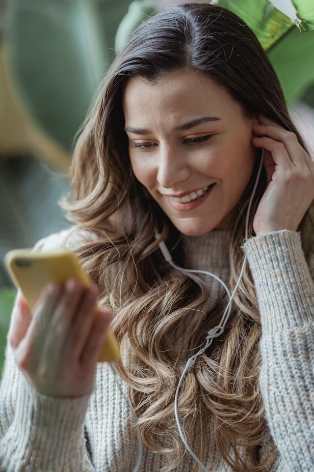 A woman uses a phone with earphones connected.
