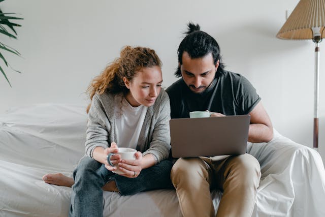 A couple sits on the couch and watches videos on a laptop.