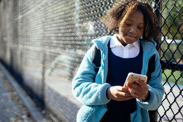 A young girl watches something on her cellphone screen.
