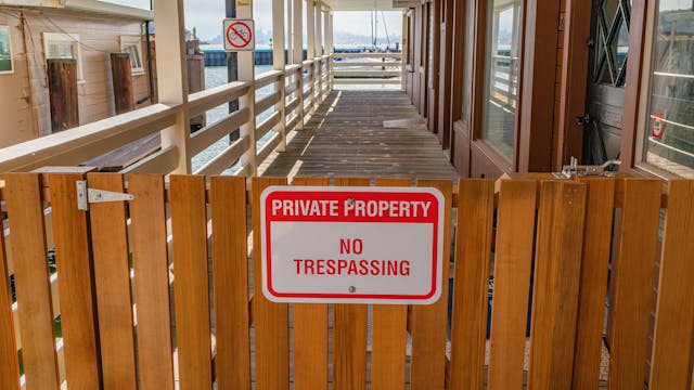 A wooden gate with a red and white sign that says, “Private property, no trespassing.”