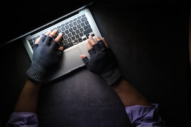 An anonymous person wears gloves and types on a laptop.