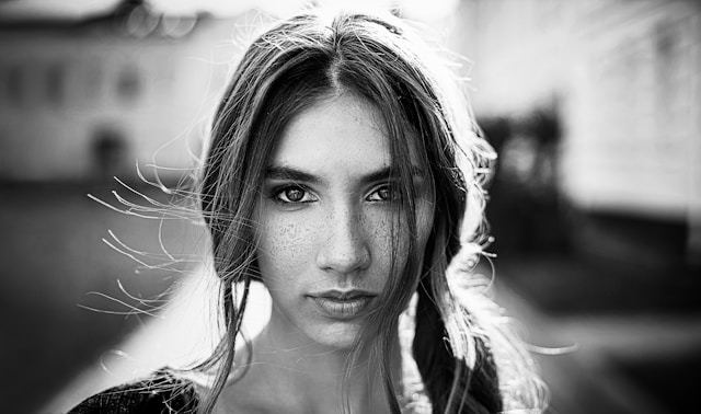 A woman with freckles and long hair looks straight at the camera.
