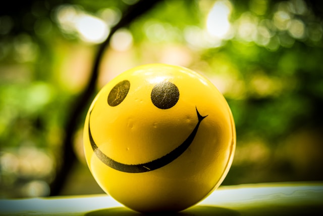 A yellow stress ball has a smiling emoji printed on it.