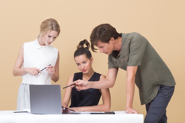 Three professionals gather around a laptop and discuss their TikTok strategy.