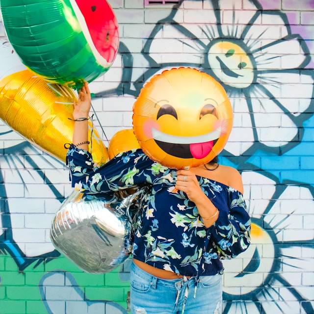 A woman holds a yellow smiley balloon in front of her face.