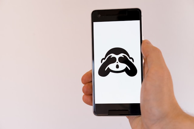 A phone screen displays a monkey with its hands over its eyes.