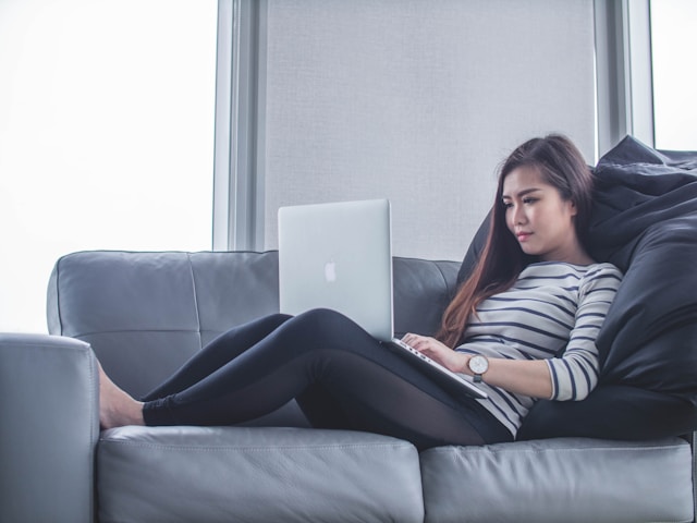 A woman lies on a couch while she uses her laptop.
