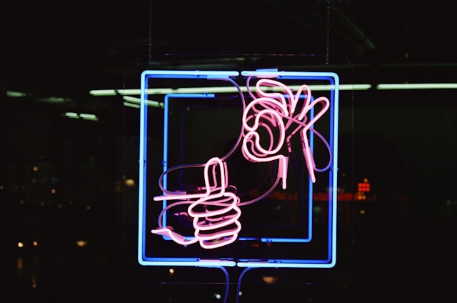 A red neon sign shows one hand giving a thumb up and another hand making the okay sign.