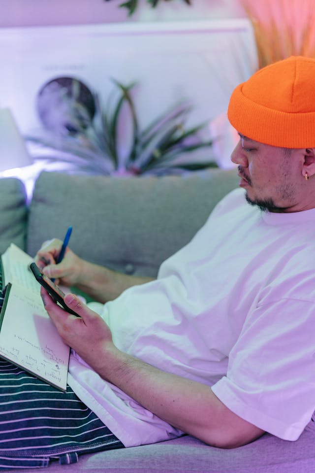 A man makes notes while scrolling his phone.