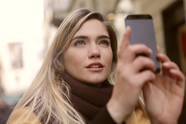 A woman holds up her phone to record something in the distance.