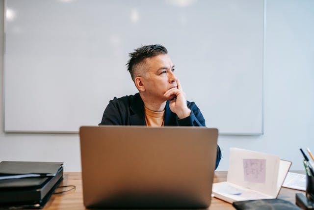 A man in deep thought sits in front of his laptop.