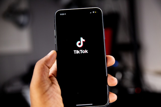 A person holds a black cellphone displaying the TikTok logo.
