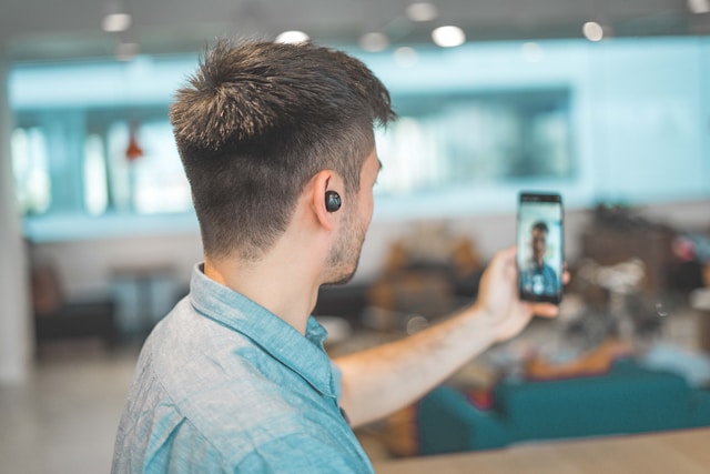 A man wears wireless earphones and makes a video call with his phone.