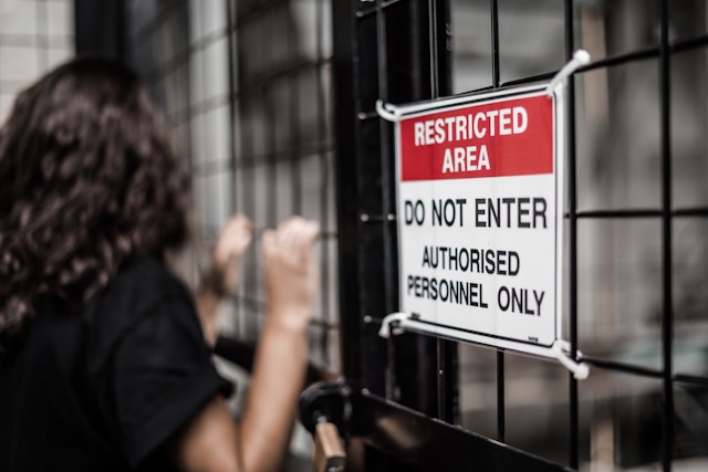 A person grabs a metal gate with a red, black, and white Restricted sign on it.