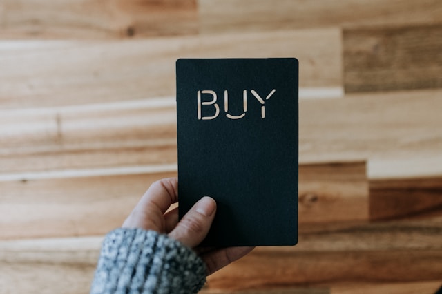 A person holds a black card with the word “BUY” on it.