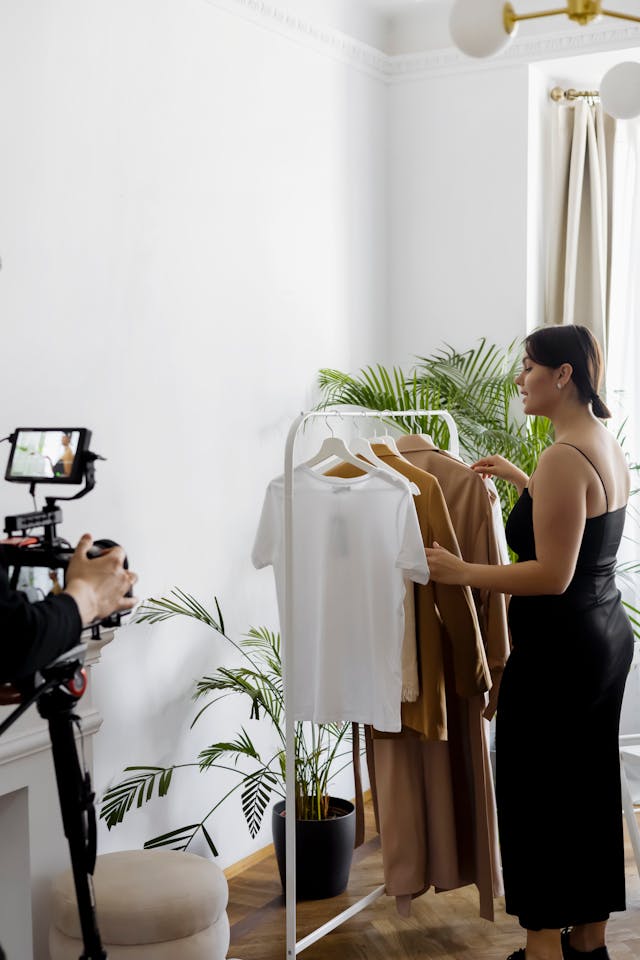 A woman records a video showing off a rack of clothing.