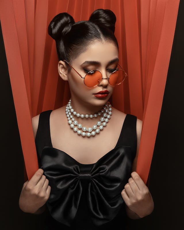 A woman wears a large bow top and pearl necklace.