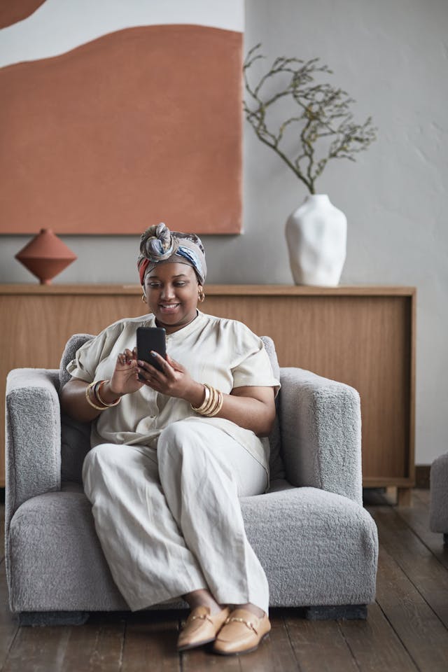 A woman with a headwrap uses her phone on a couch.