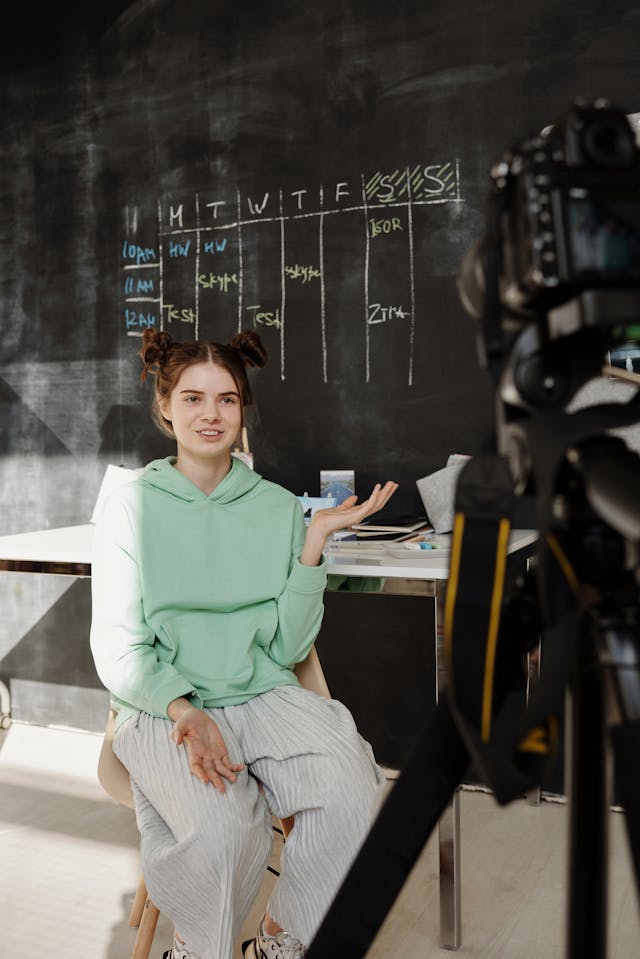 A girl in a green hoodie talks to a camera.