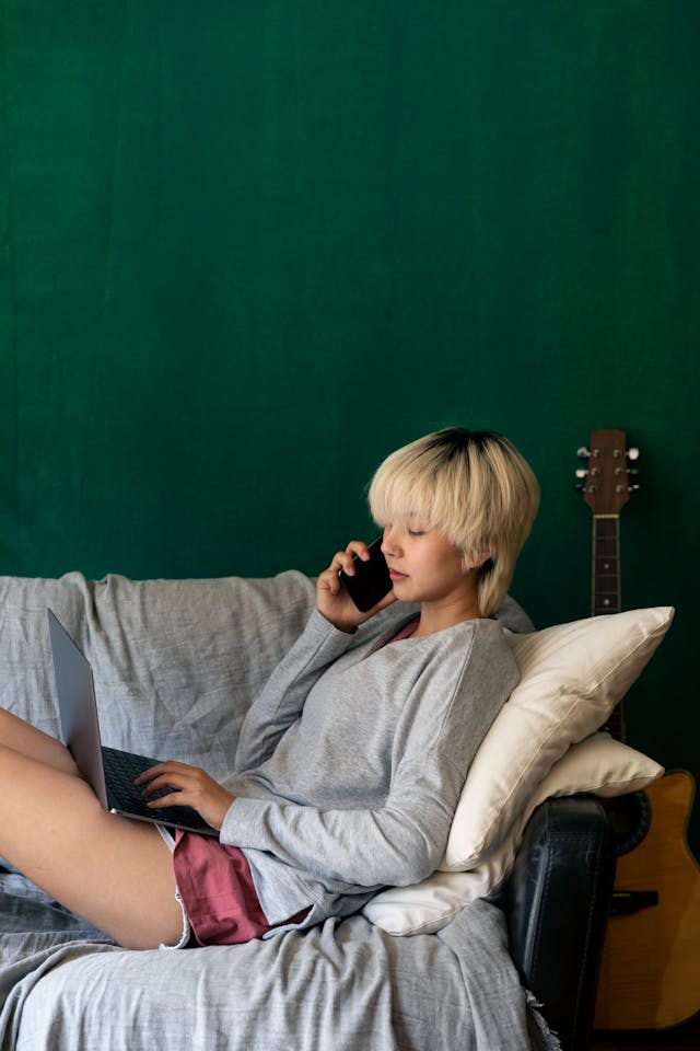 A woman using her cell phone while typing on a laptop.