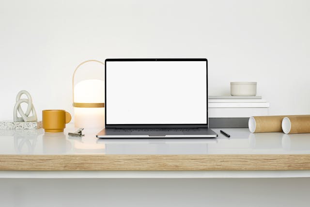 A MacBook, pen, and cup on a white surface.