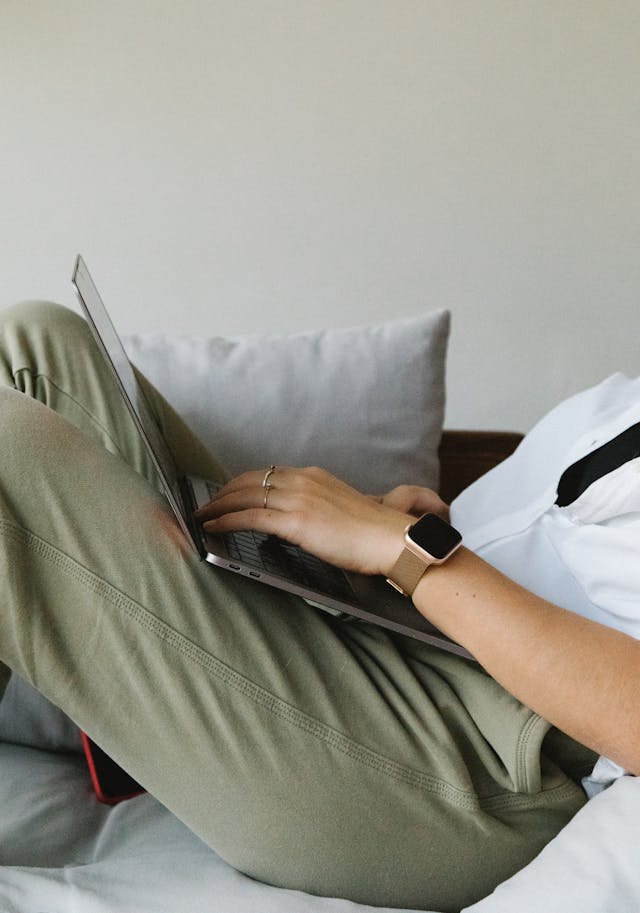 A person uses a laptop while sitting on a couch.