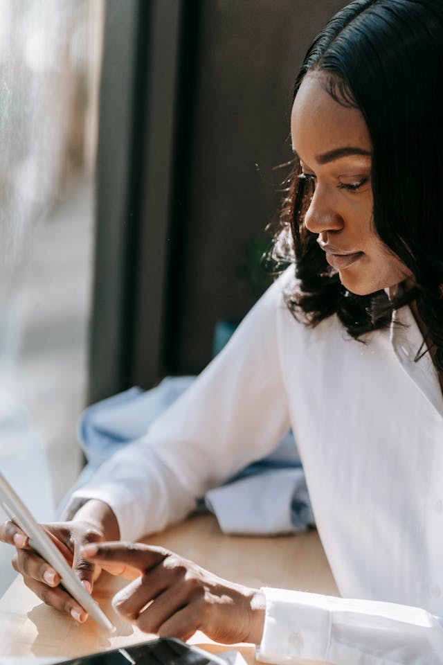 A woman in a white blouse taps her phone screen.
