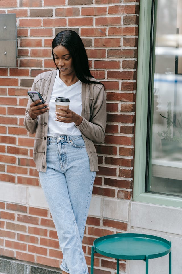 A woman looks down at her phone while holding a cup of coffee.