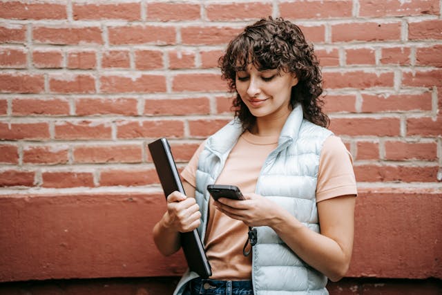 A woman smiles as she looks at her cell phone.