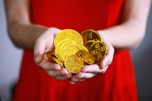 A woman in a red dress holds gold coins in her hands.