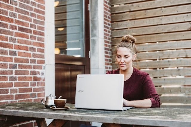A woman sits at an outdoor table and schedules TikTok posts on her laptop.