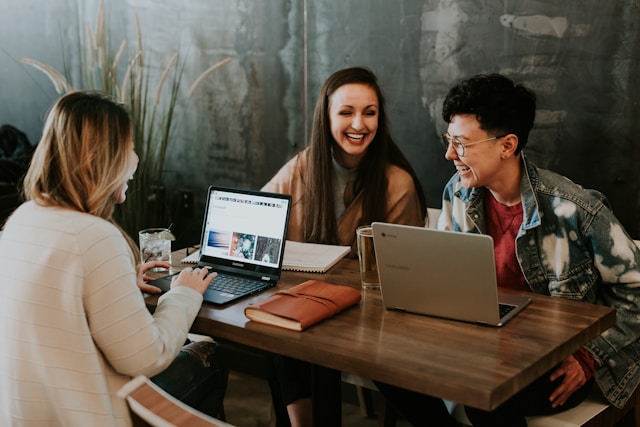 A group of young professionals sit around a table in front of their laptops and discuss social media content strategies.