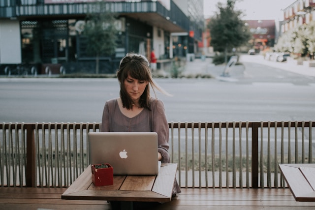 A woman types on a laptop in front of an empty street.