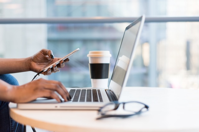 A person checks their phone while browsing on their laptop.