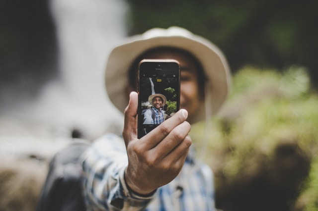 An influencer takes a selfie outdoors with their phone.